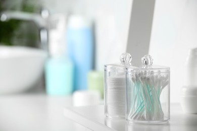 Photo of Containers with cotton swabs and pads on white shelf in bathroom. Space for text