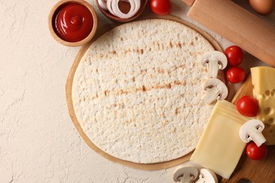 Photo of Pizza base, ketchup and products on light textured table, flat lay. Space for text