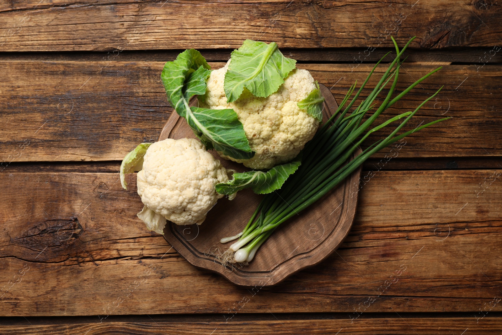 Photo of Fresh raw cauliflower cabbages and green onions on wooden table, top view