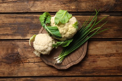 Fresh raw cauliflower cabbages and green onions on wooden table, top view