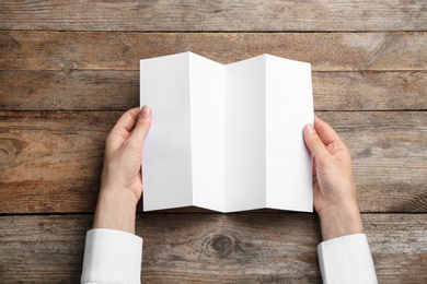 Young woman holding blank brochure at wooden table, top view. Mock up for design