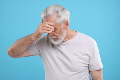 Photo of Embarrassed senior man covering eyes on light blue background