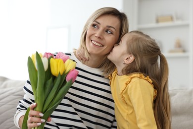 Photo of Little daughter kissing and congratulating her mom with Mother`s Day at home. Woman holding bouquet of beautiful tulips