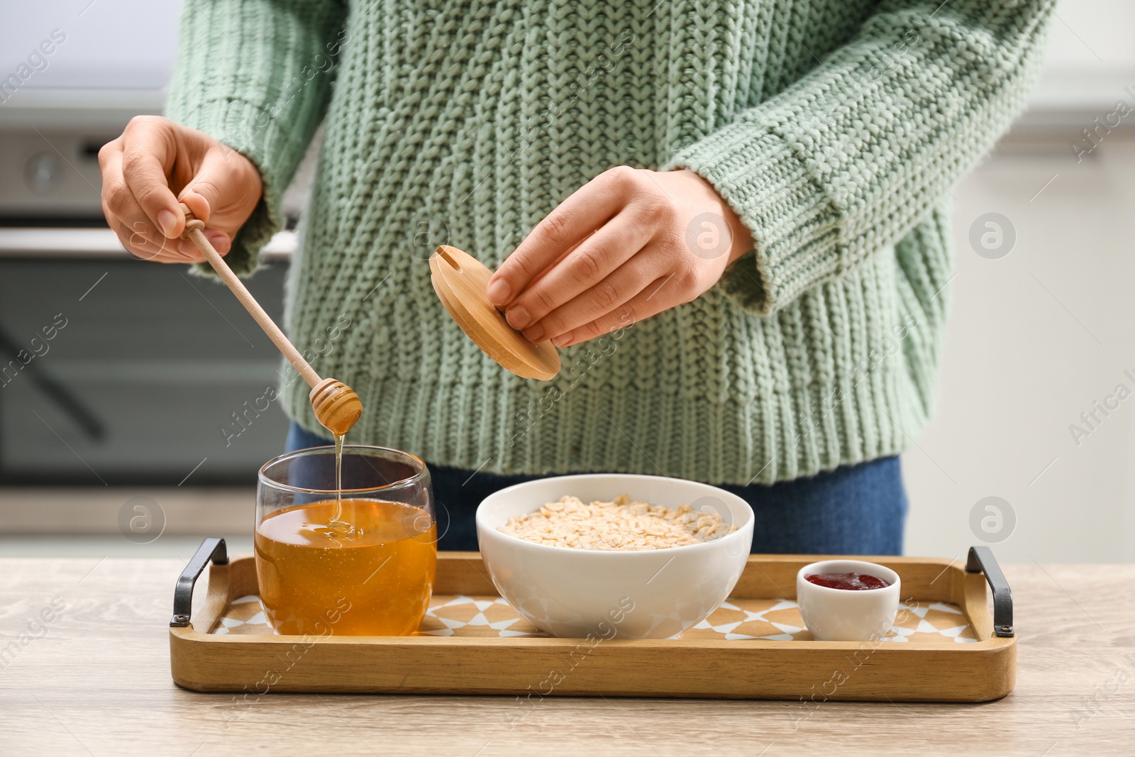 Photo of Woman adding honey to oatmeal at wooden table indoors, closeup
