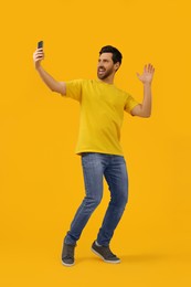 Happy man taking selfie with smartphone on yellow background, space for text