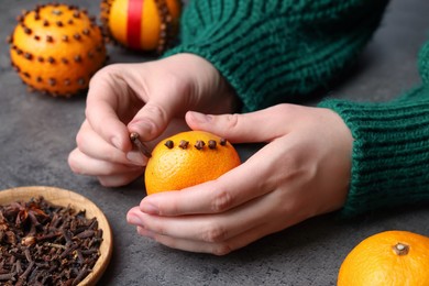 Woman decorating fresh tangerine with cloves at grey table, closeup