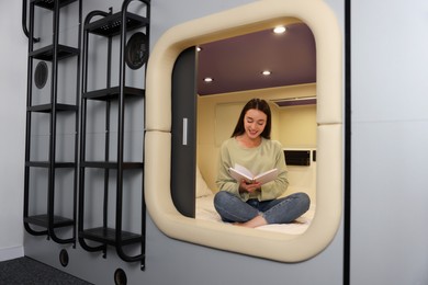 Happy young woman reading book in capsule of pod hostel
