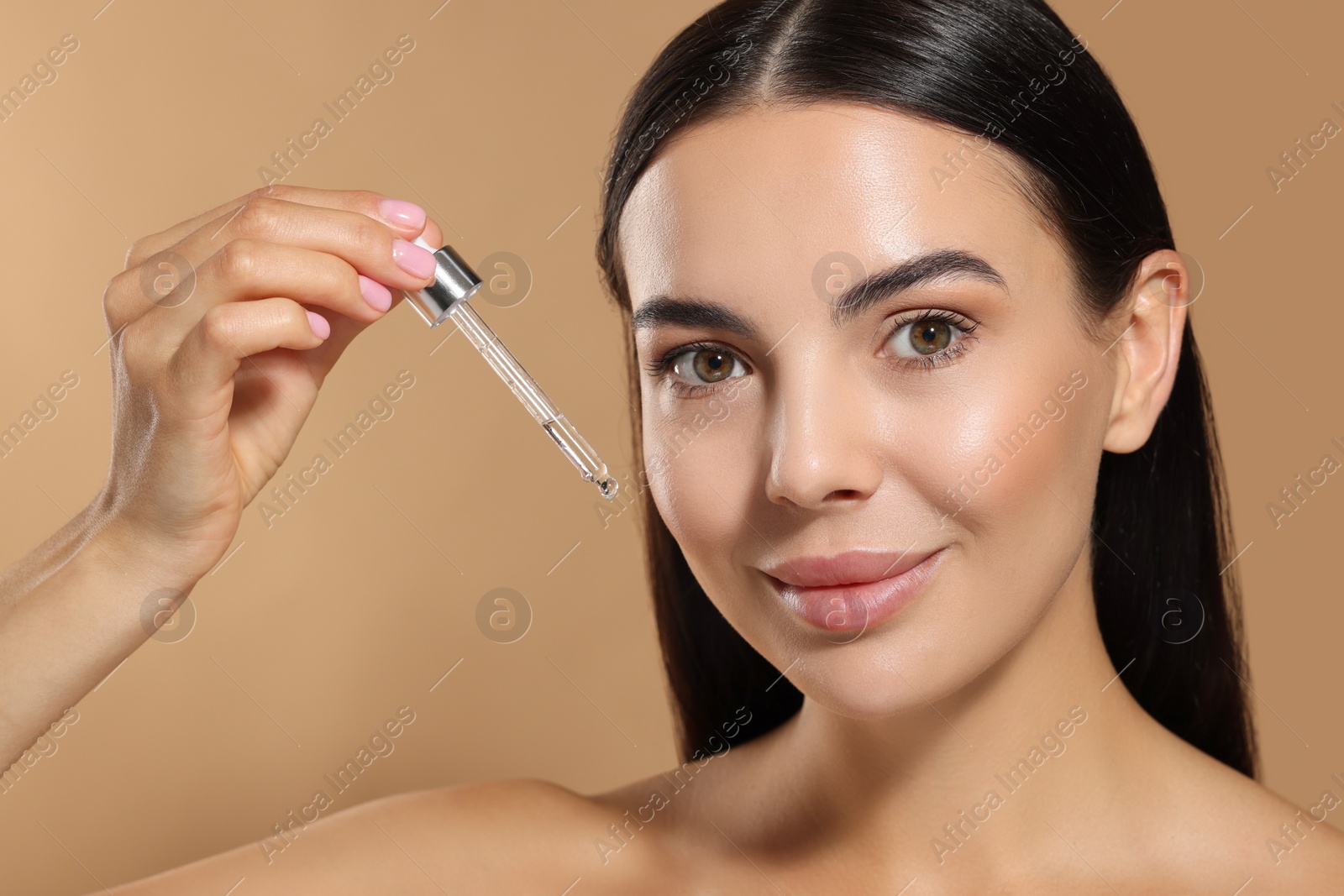 Photo of Beautiful young woman applying serum onto her face on beige background