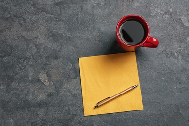 Photo of Clean napkin, cup of coffee and pen on grey background, top view with space for text