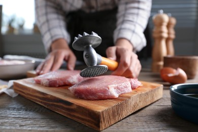 Photo of Woman cooking schnitzel at wooden table indoors, selective focus