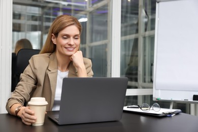 Photo of Woman with cup of coffee working on laptop at black desk in office. Space for text