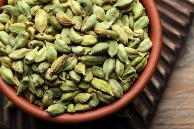 Bowl of dry cardamom pods on wooden table, closeup