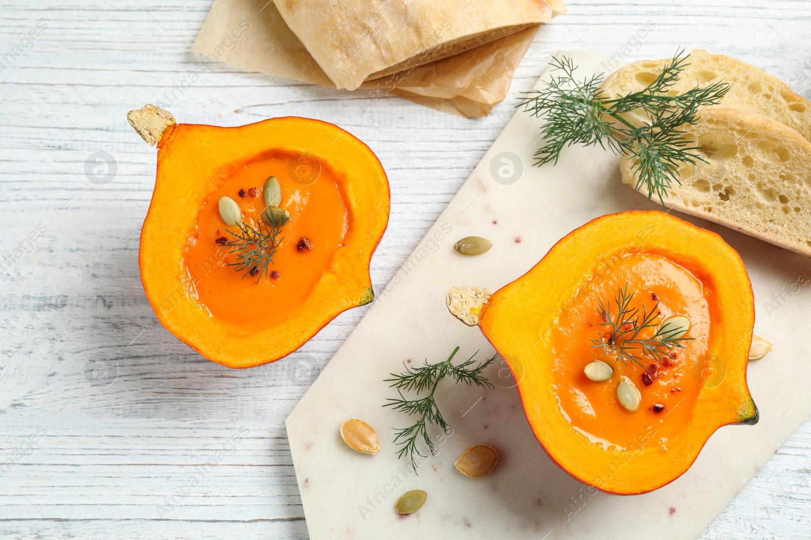 Photo of Tasty cream soup in pumpkin halves on white wooden table, flat lay