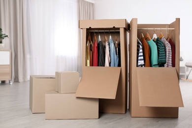 Photo of Cardboard wardrobe boxes with clothes on hangers indoors. Space for text