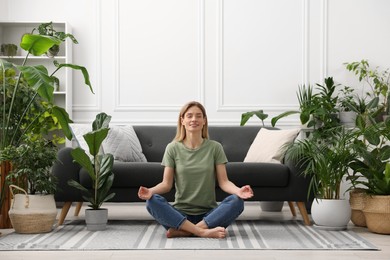 Woman meditating surrounded by beautiful potted houseplants at home