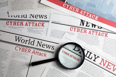 Photo of Newspaper with headline CYBER ATTACK and magnifying glass, top view