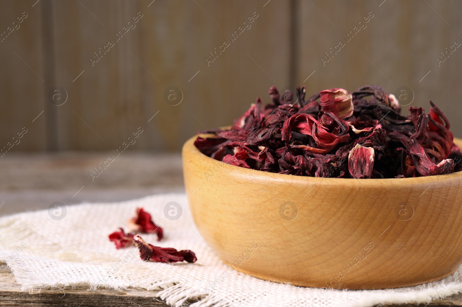 Photo of Dry hibiscus tea in bowl on wooden table, closeup. Space for text