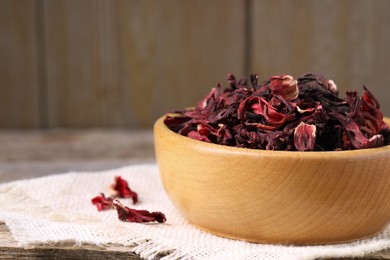 Dry hibiscus tea in bowl on wooden table, closeup. Space for text