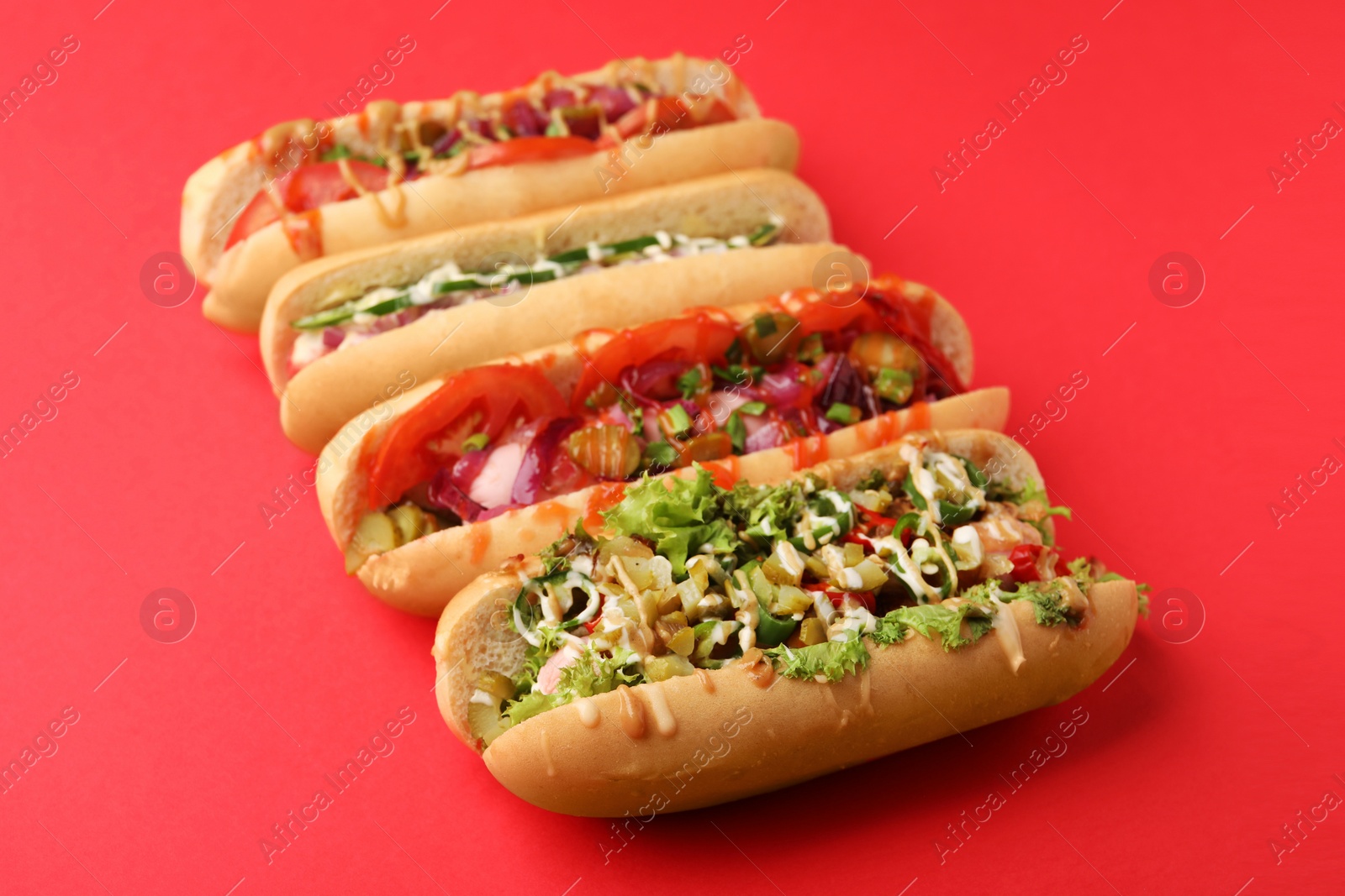 Photo of Delicious hot dogs with different toppings on red background
