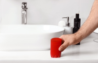 Photo of Man holding stick deodorant in bathroom, closeup view. Space for text