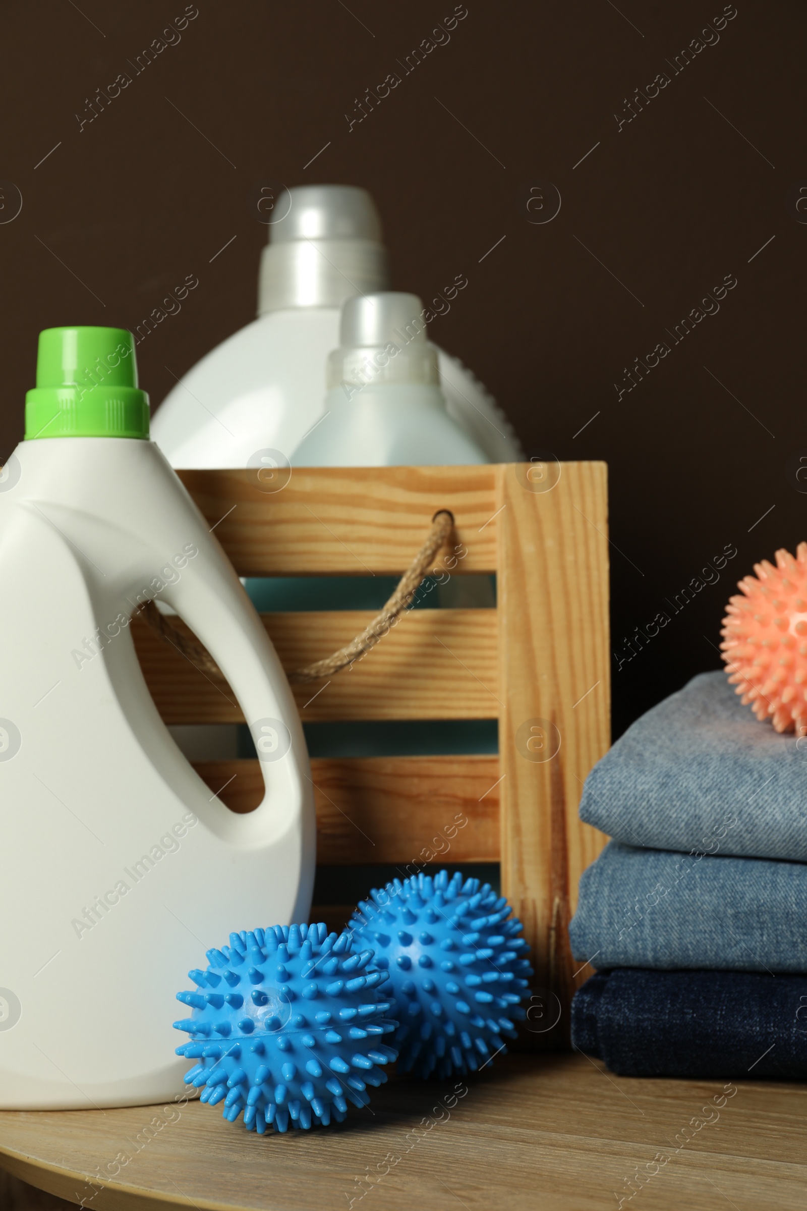 Photo of Many dryer balls, stacked clean clothes and laundry detergents on wooden table