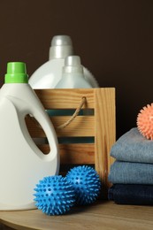 Photo of Many dryer balls, stacked clean clothes and laundry detergents on wooden table