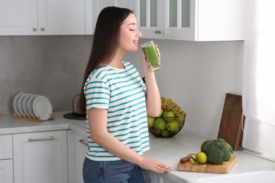 Photo of Beautiful young woman drinking tasty smoothie in kitchen