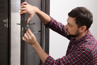 Handsome handyman repairing door lock in room