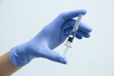 Photo of Doctor holding syringe with COVID-19 vaccine on light background, closeup