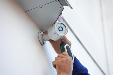 Photo of Technician installing CCTV camera on wall outdoors, closeup
