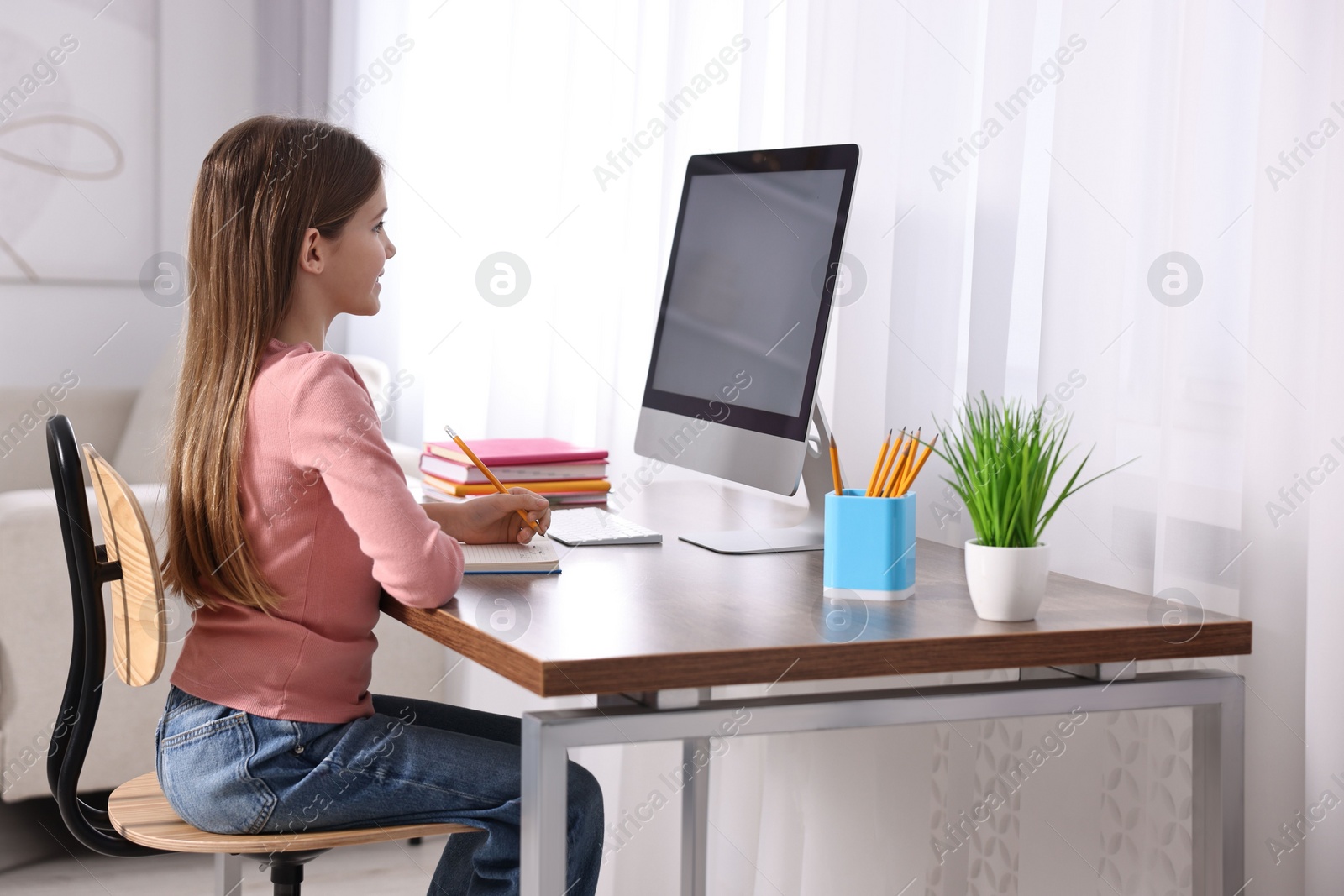 Photo of E-learning. Girl taking notes during online lesson at table indoors