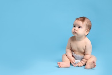 Photo of Cute little baby in diaper sitting on light blue background. Space for text