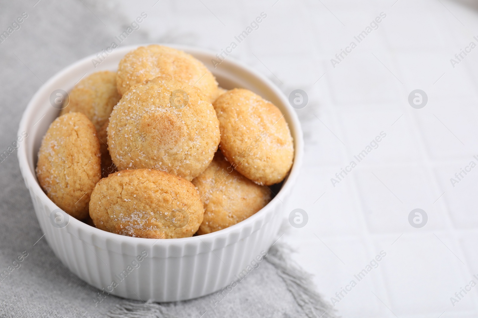 Photo of Tasty sugar cookies in bowl on white tiled table, closeup. Space for text