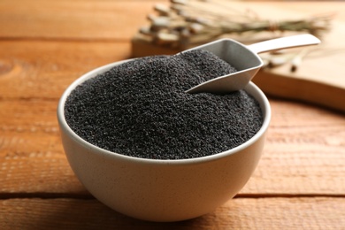 Poppy seeds and scoop in bowl on wooden table