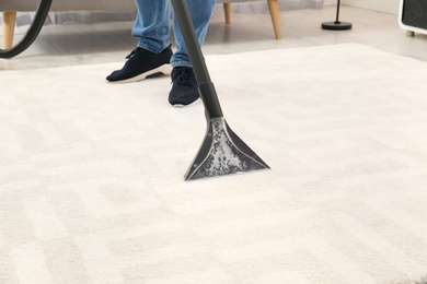 Man removing dirt from carpet with vacuum cleaner indoors, closeup