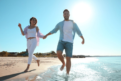 Happy young couple running on beach near sea, low angle view. Honeymoon trip