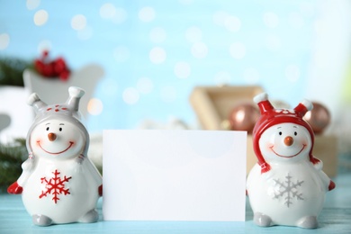 Decorative snowmen near blank white card on light blue table, space for text