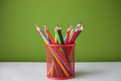 Many colorful pencils in holder on light table against green background