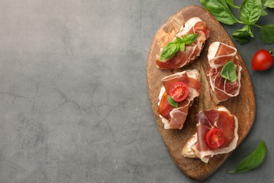 Tasty sandwiches with cured ham, basil and tomatoes on grey textured table, flat lay. Space for text