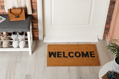 Photo of Doormat with word Welcome near shoe rack on white wooden floor in hall