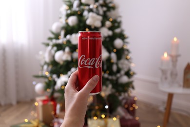 MYKOLAIV, UKRAINE - JANUARY 13, 2021: Woman holding can of Coca-Cola in room with Christmas tree, closeup