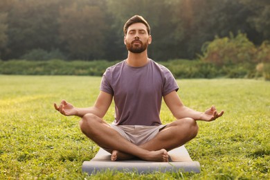 Photo of Man practicing yoga on mat outdoors. Lotus pose