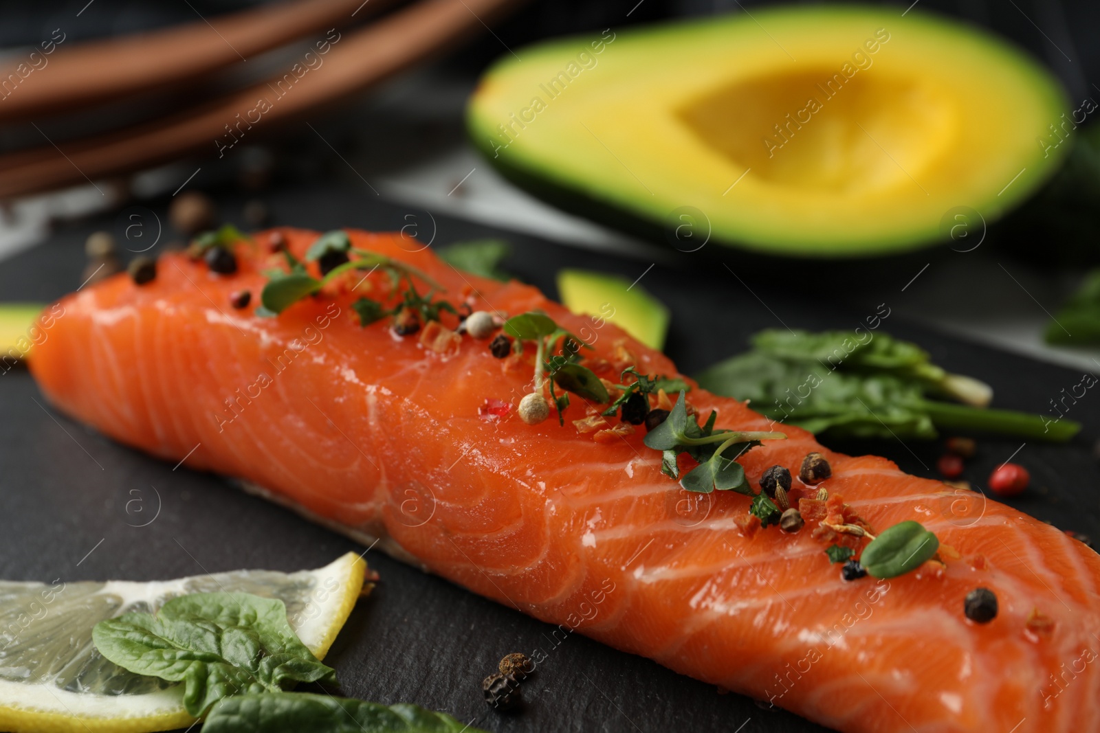 Photo of Delicious salmon served with spinach and lemon on slate board, closeup