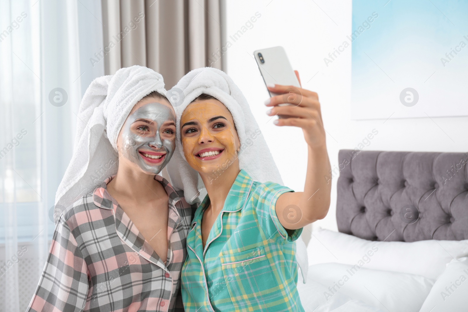 Photo of Young friends with facial masks taking selfie in bedroom at pamper party