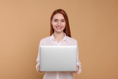 Smiling young woman with laptop on beige background