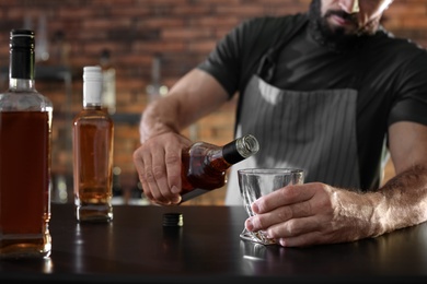 Photo of Bartender pouring whiskey into glass at counter in bar, closeup. Space for text