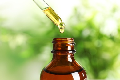 Photo of Dripping natural tea tree essential oil into bottle on blurred background, closeup