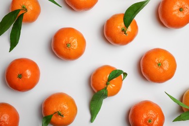 Photo of Delicious tangerines and green leaves on white background, flat lay