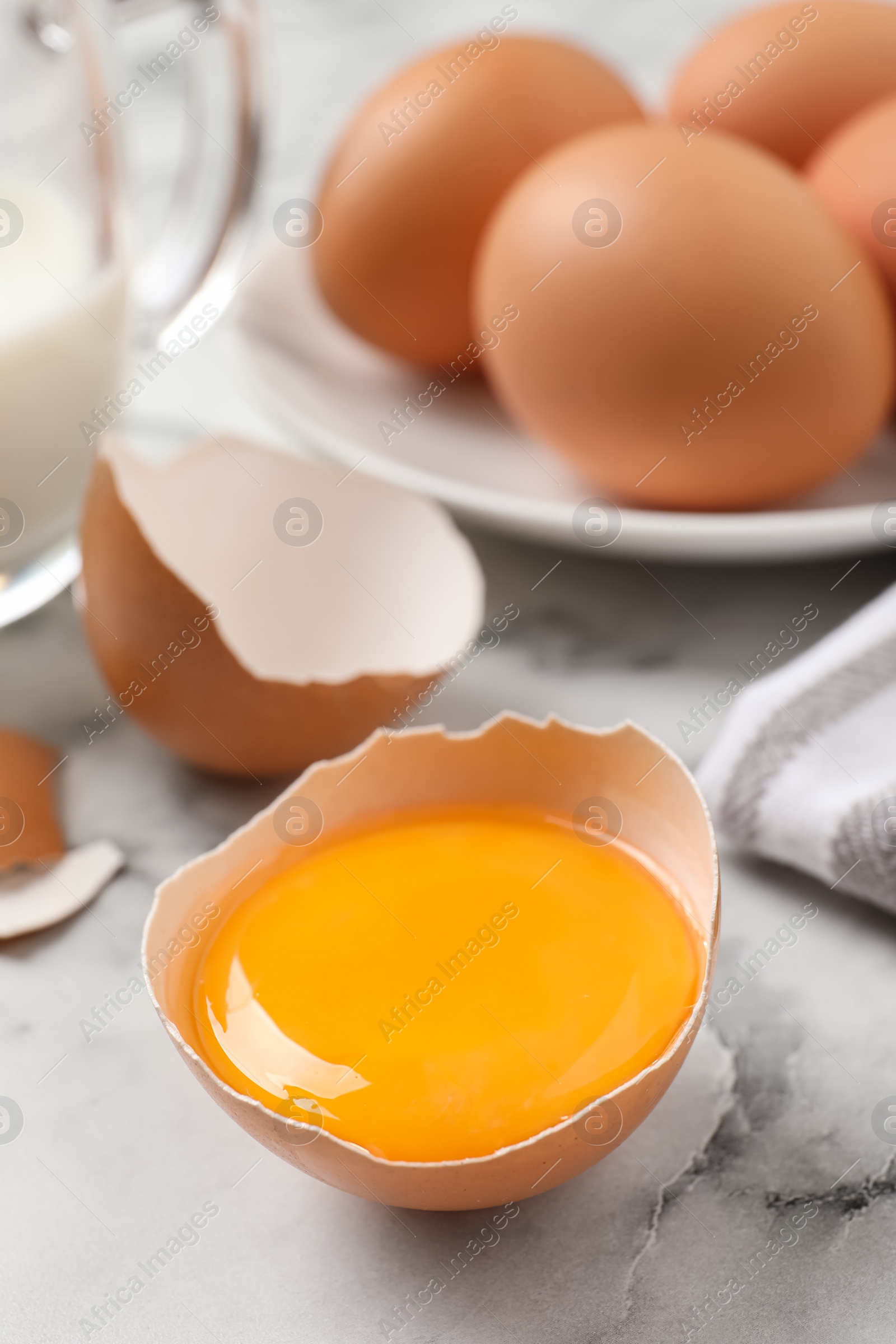 Photo of Cracked eggshell with raw yolk on white marble table, closeup. Space for text