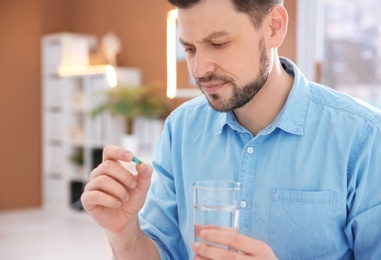 Photo of Young man with pill and glass of water indoors